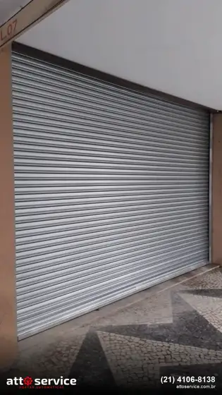 Porta de enrolar cinza de grande vão em fachada comercial