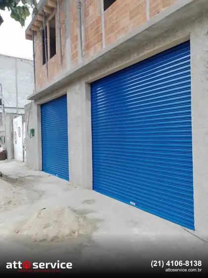 Obra em alvenaria com porta social azul ao lado da porta grande de garagem